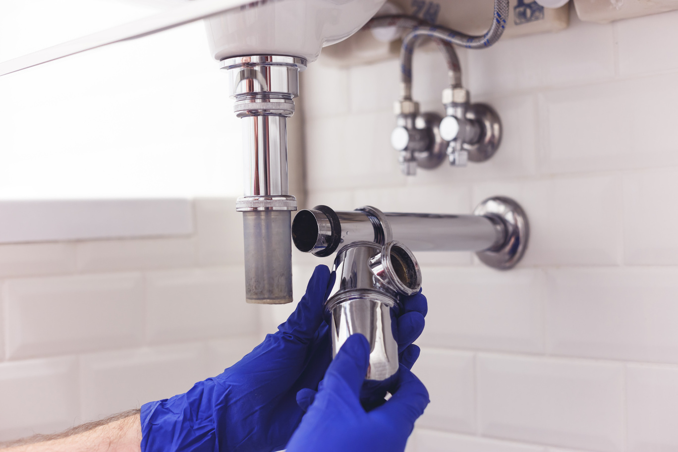 Plumber repairs and maintains chrome siphon under the washbasin. Plumber at work in bathroom, plumbing assemble and install concept plumber repairing piping on bathroom sink