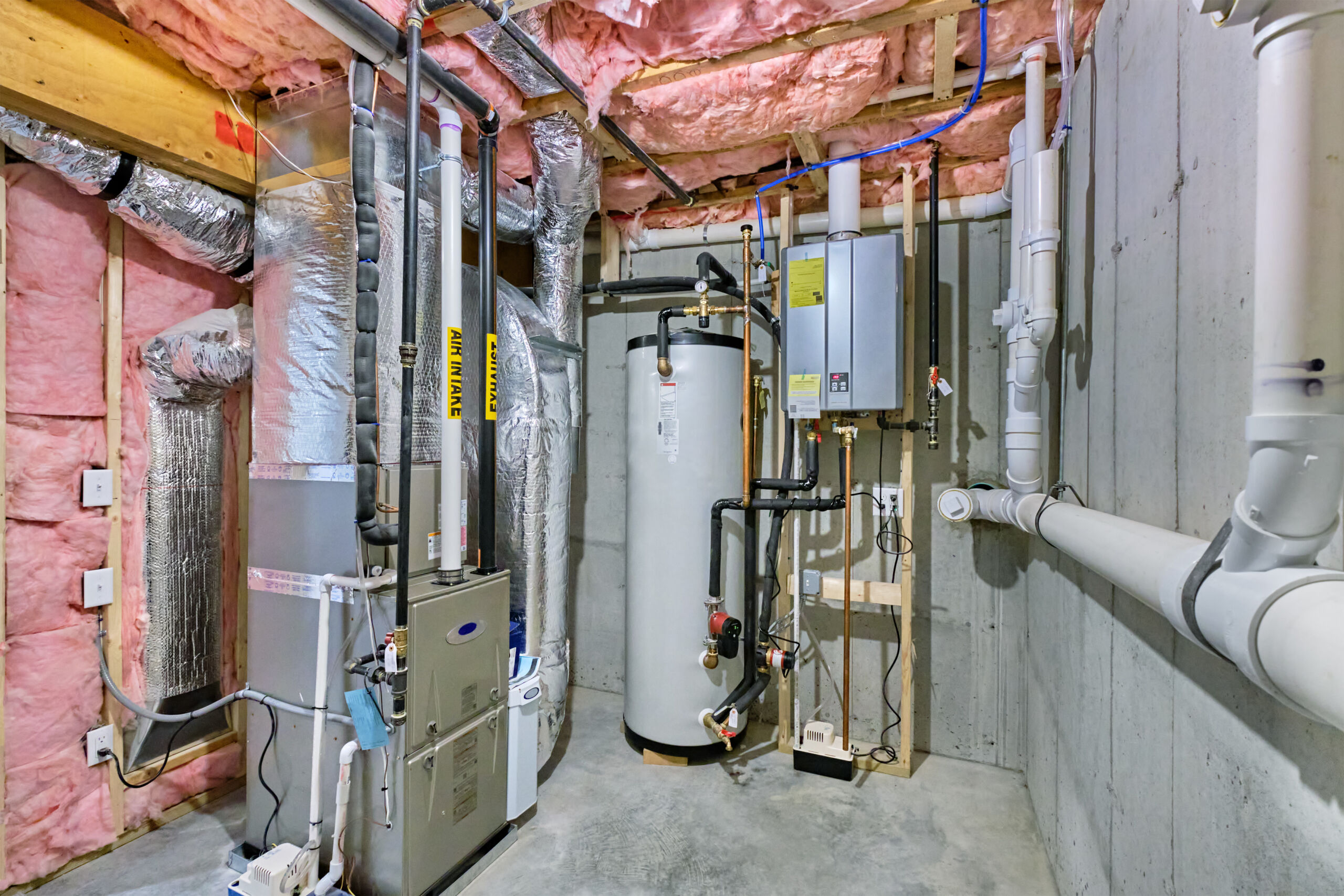 Unfinished basement mechanical room with condensing tankless water heater, storage tank, plumbing and heating systems plumbing in an unfinished basement