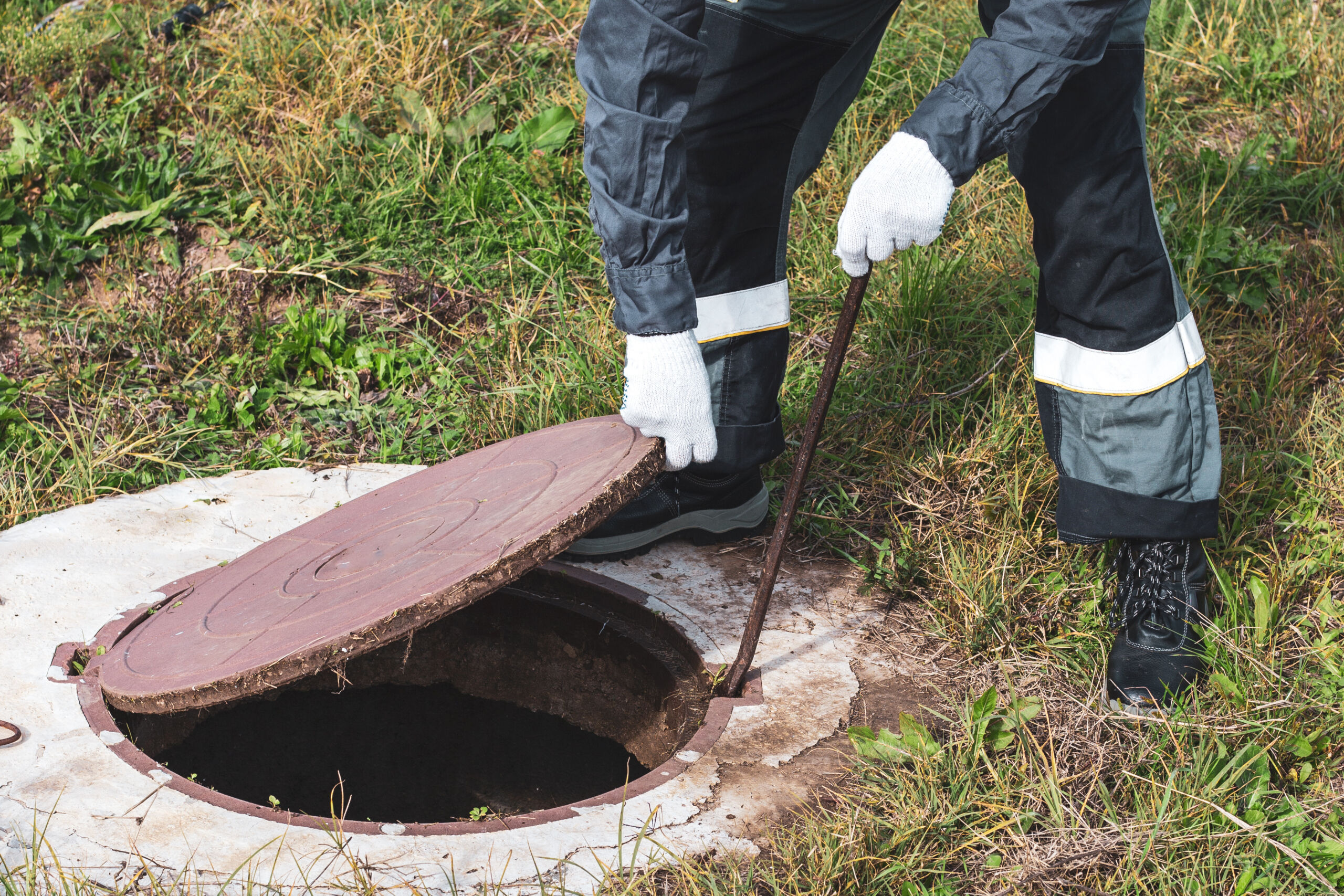 On a septic sewer well, a worker opens the manhole cover. Plumbing work sewer line repair