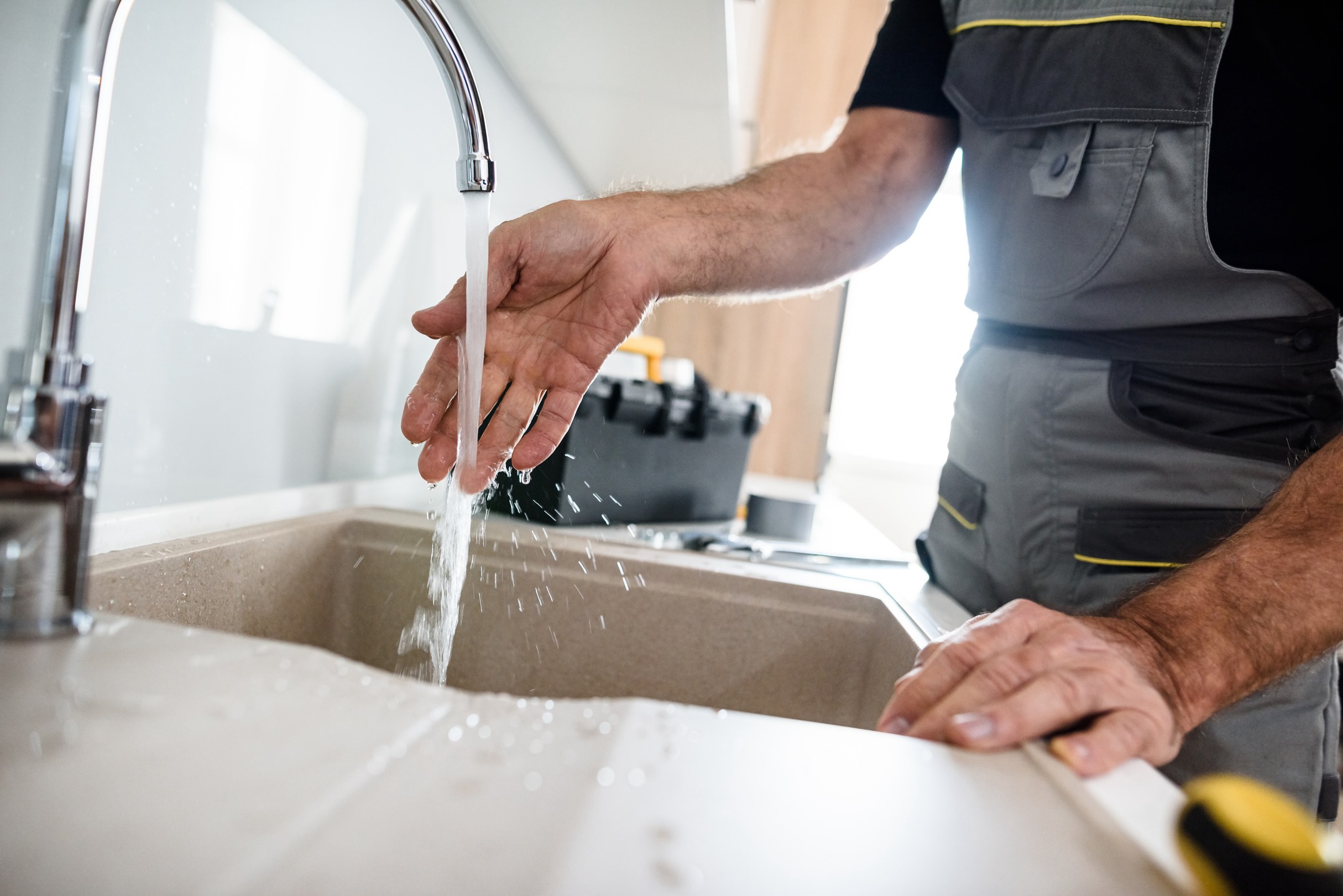 Close up of hands of aged repairman in uniform working, checking water stream, fixing broken kitchen tap. Repair service concept plumbing fixture installation